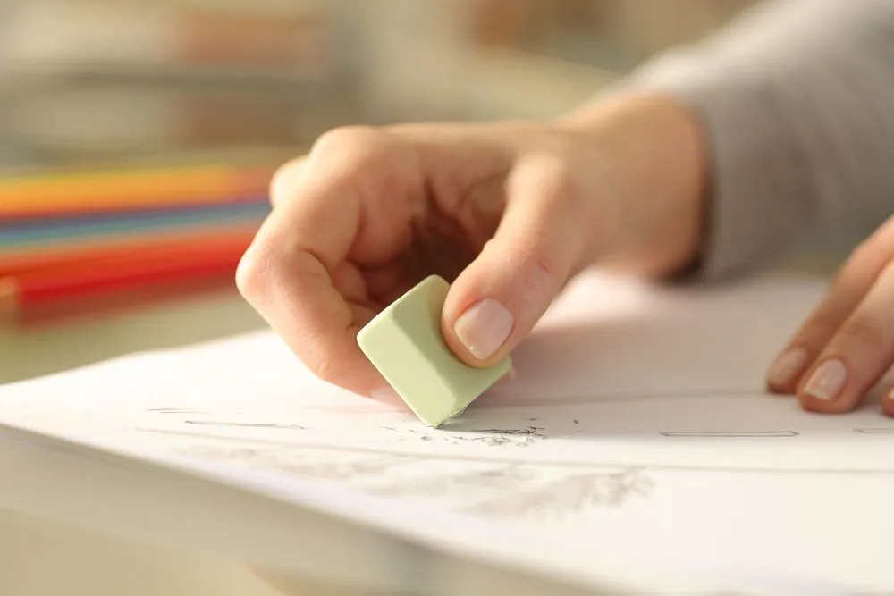 Woman using an eraser to rub off a pencil sketch (Credits: Pheelings media/Shutterstock)