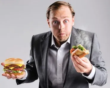 Busy businessman eating takeaway sandwich on the go, shrugging to the fast pace of life cold & hot food