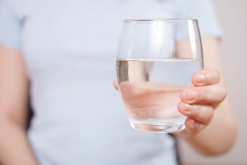 Woman is hand holding drinking water on gray background - Image( Busra Ispir)S