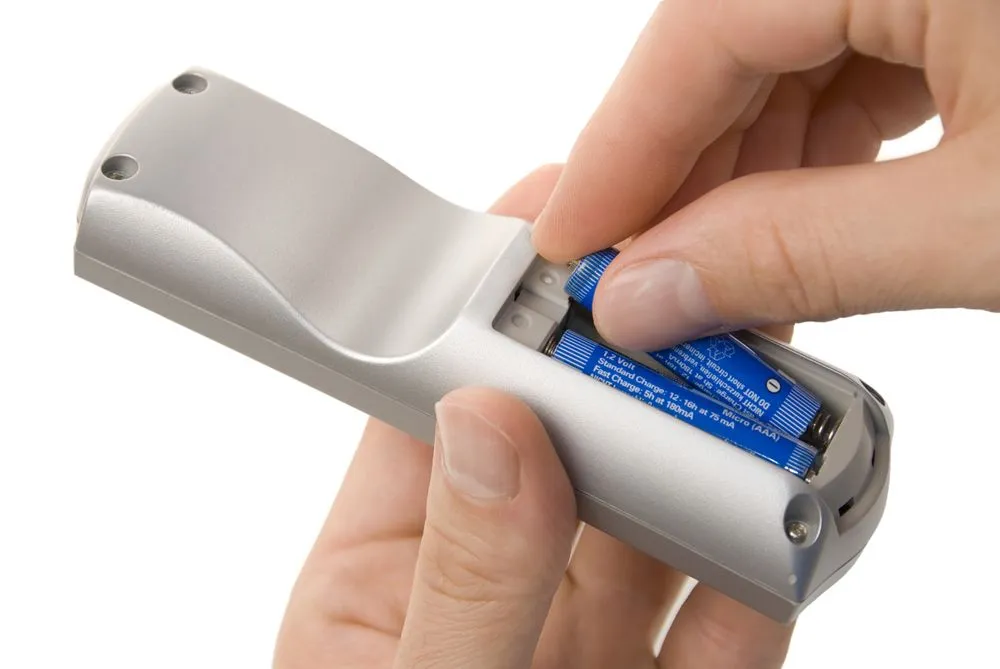 Male hands inserting batteries into a remote control, isolate on white(Smileus)s