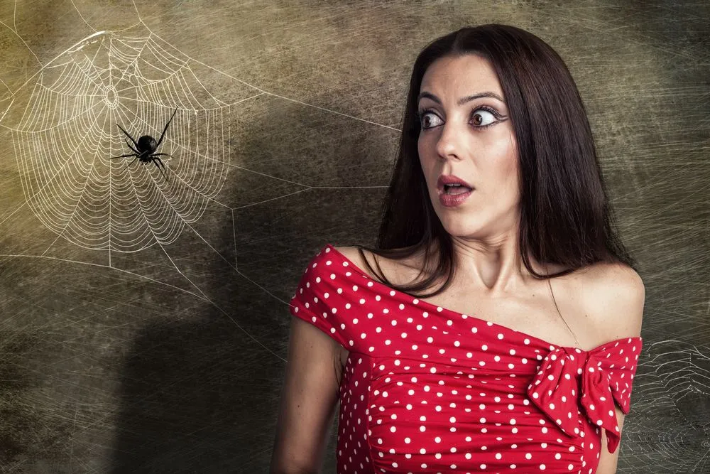 Beautiful woman is looking shocked to a spider next to her face(Cara-Foto)s