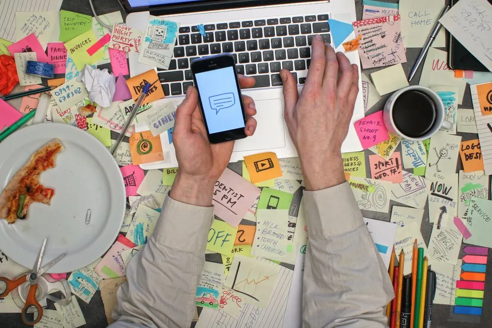Top view on man working on laptop computer with notes all around his office desk.